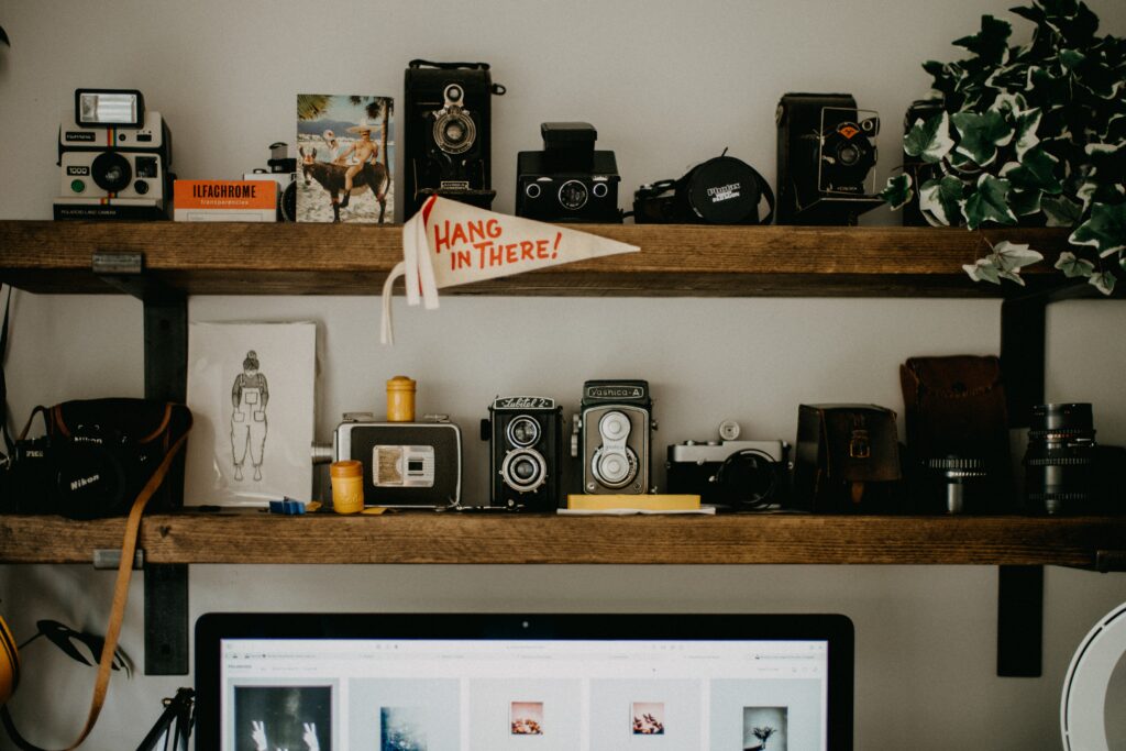 Two wooden shelves with a variety of items including cameras and a little flag saying hang in there