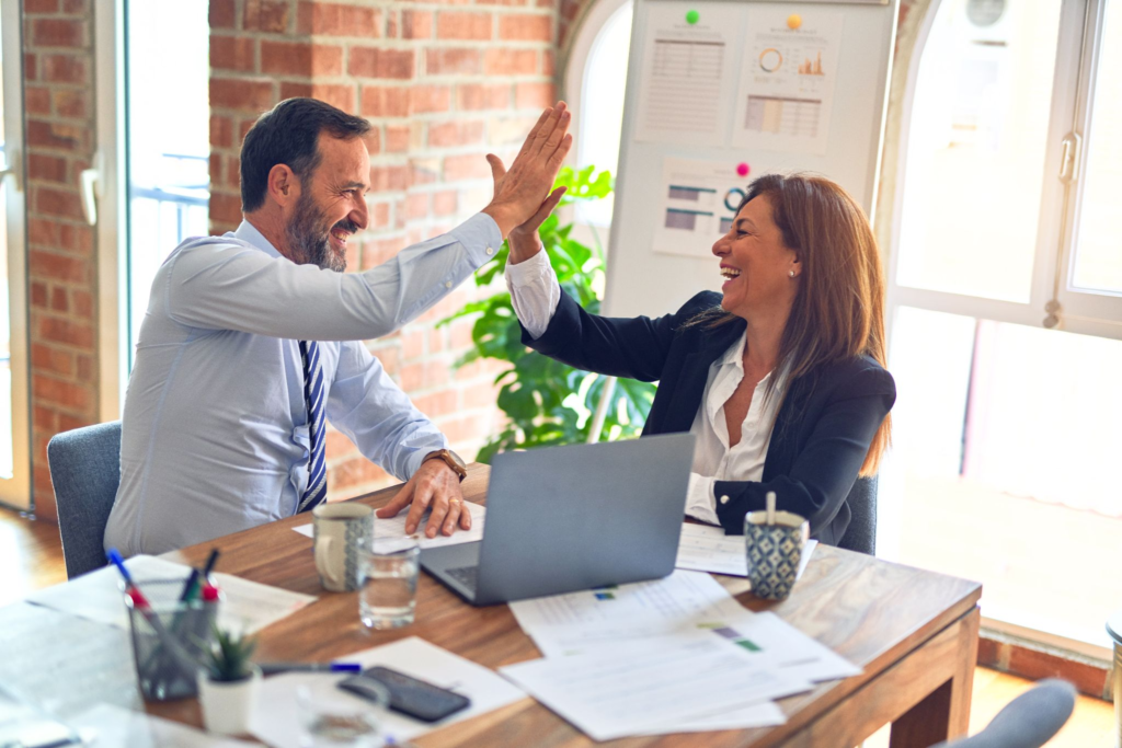 A male and a female professional giving each other a high five in an office setting